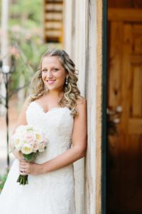 bride leaning against rustic barn holding boquet