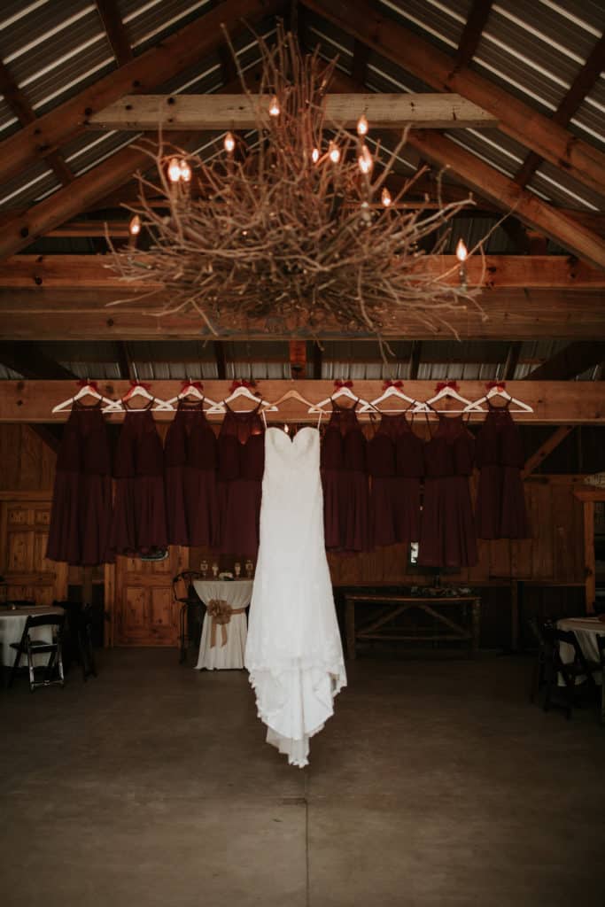 wedding dress and brides maids dresses hanging in rustic barn at vintage wedding venue in georgia